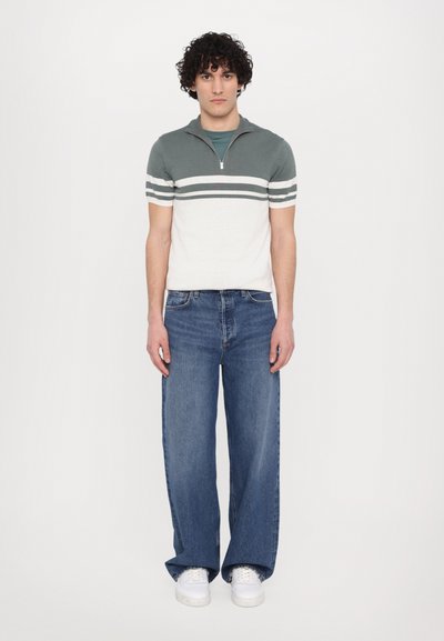 Kortärmad polo i grön och kräm, med dragkedja i kragen och horisontella ränder. Matchad med vida blå jeans och vita sneakers.