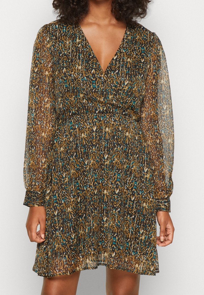 Femme portant une robe à manches longues, longueur genoux, avec un motif léopard en marron, noir et bleu sarcelle et un décolleté en V profond.