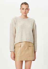 Beżowy sweter prążkowany o luźnym kroju i okrągłym dekolcie, w zestawie z dopasowaną mini spódnicą z jasnobrązowej skóry, posiadającą kieszenie z przodu.