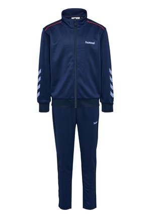 Marineblauwe trainingsoutfit met een ritsjack en bijpassende broek, voorzien van rode accenten en witte chevronpatronen op de mouwen. Gemaakt van glad, lichtgewicht materiaal.