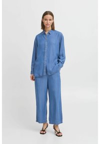 Camicetta in denim blu chiaro con bottoni frontali, maniche lunghe e colletto, abbinata a pantaloni in denim a gamba larga dello stesso colore.