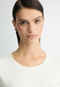 Witte top met korte mouwen, voorzien van een ronde halslijn, versierd met textuurpunten die in een zonnestraalpatroon rond de kraag zijn gerangschikt.