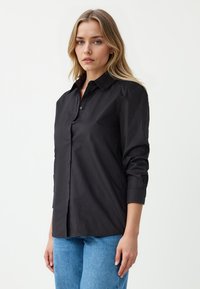 Zwarte button-up shirt met een kraag, lange mouwen opgerold bij de manchetten, gemaakt van een gladde stof. Heeft een rechte snit en een minimalistisch ontwerp.