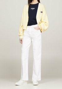 Cárdigan amarillo de canalé sobre una camiseta azul marino con letras blancas, combinado con jeans blancos de cintura alta y zapatillas blancas.