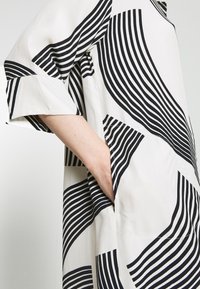 Tunic a righe ondulate bianco e nero, con maniche corte, tessuto leggero e tasche laterali per una maggiore funzionalità.