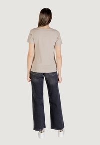 T-shirt in cotone beige con maniche corte, abbinato a jeans in denim scuro a gamba larga e sneakers bianche. Design semplice, texture liscia.