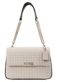 Beżowa pikowana torebka z czarnym obszyciem, srebrnym łańcuszkowym paskiem i tabliczką z logo. Posiada zapięcie na klapę oraz mały ozdobny tag.