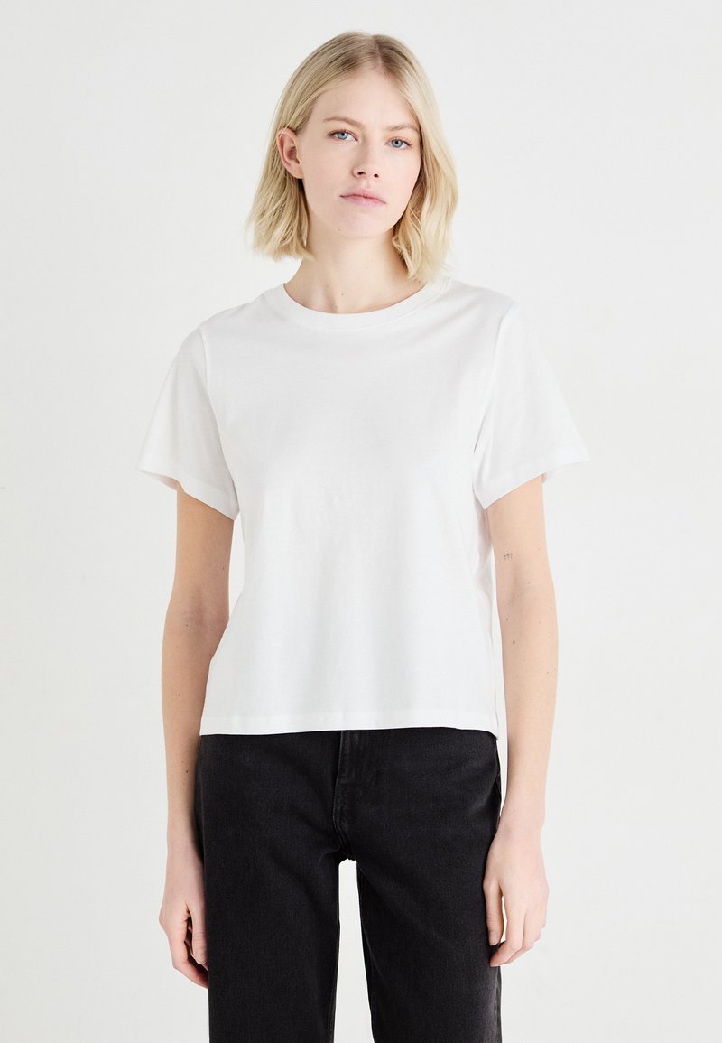 T-shirt en coton blanc à manches courtes, avec un col rond et une coupe décontractée, associé à un jean noir. Design minimaliste, texture lisse.