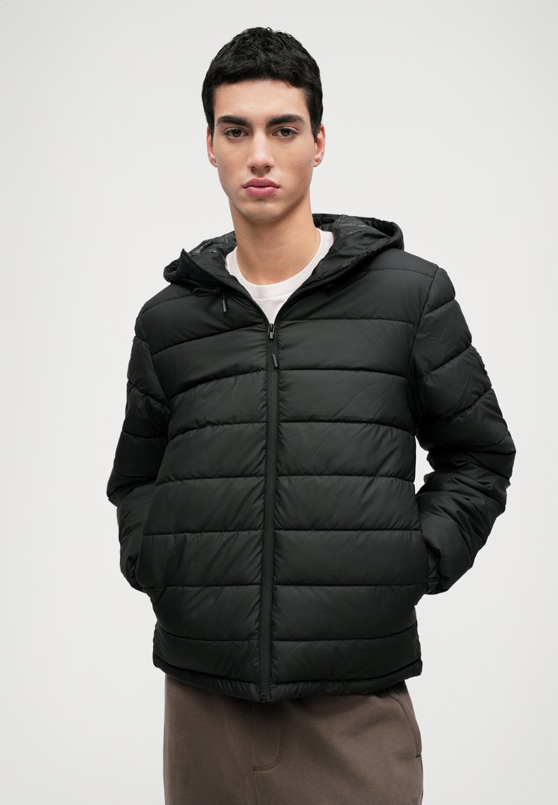 Veste en duvet noire avec un design à carreaux horizontaux, fermeture éclair et capuche ajustable. Texture lisse et isolation légère.