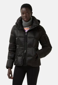 Černá péřová bunda s kapucí, prošívaný design, přední zip a boční kapsy. Pod tím je silný pletený šedý rolák.
