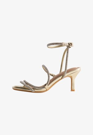 Gold high-heeled sandal with thin, rhinestone-embellished straps around toes and ankle, and a small buckle closure.