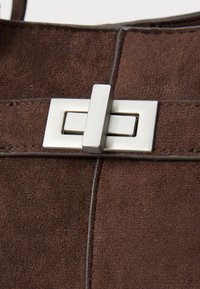 Braune Wildleder-Handtasche mit einem rechteckigen silbernen Metallverschluss und gesteppten Akzenten an den Seiten. Glatte Textur mit matter Oberfläche.