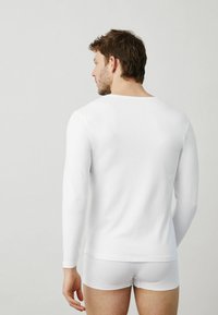 Camisa blanca de manga larga con cuello redondo, combinada con braguitas blancas. Presenta un tejido suave y liso con un diseño ajustado.