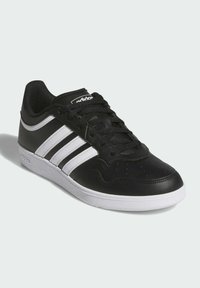 Zapatillas de cuero negro con acentos blancos, que cuentan con un acabado texturizado, punta redondeada y un clásico diseño de tres franjas en el lateral.