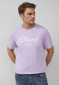 Lawendowa koszulka z krótkim rękawem z okrągłym dekoltem, z białym nadrukiem "s.Oliver ELEVATED ESSENTIALS SINCE 1969". Gładki materiał bawełniany.