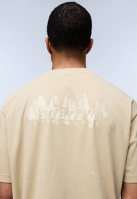 Camiseta de algodón beige con un gráfico de temática natural impreso en la parte posterior. Mangas cortas, cuello redondo y textura suave.