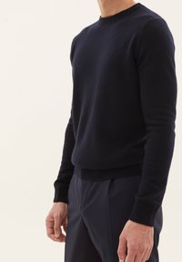 Marineblauer Rundhalsausschnitt-Pullover aus weichem, strukturiertem Strick; taillierte Passform mit gerippten Bündchen und Saum, kombiniert mit dunklen Hosen.