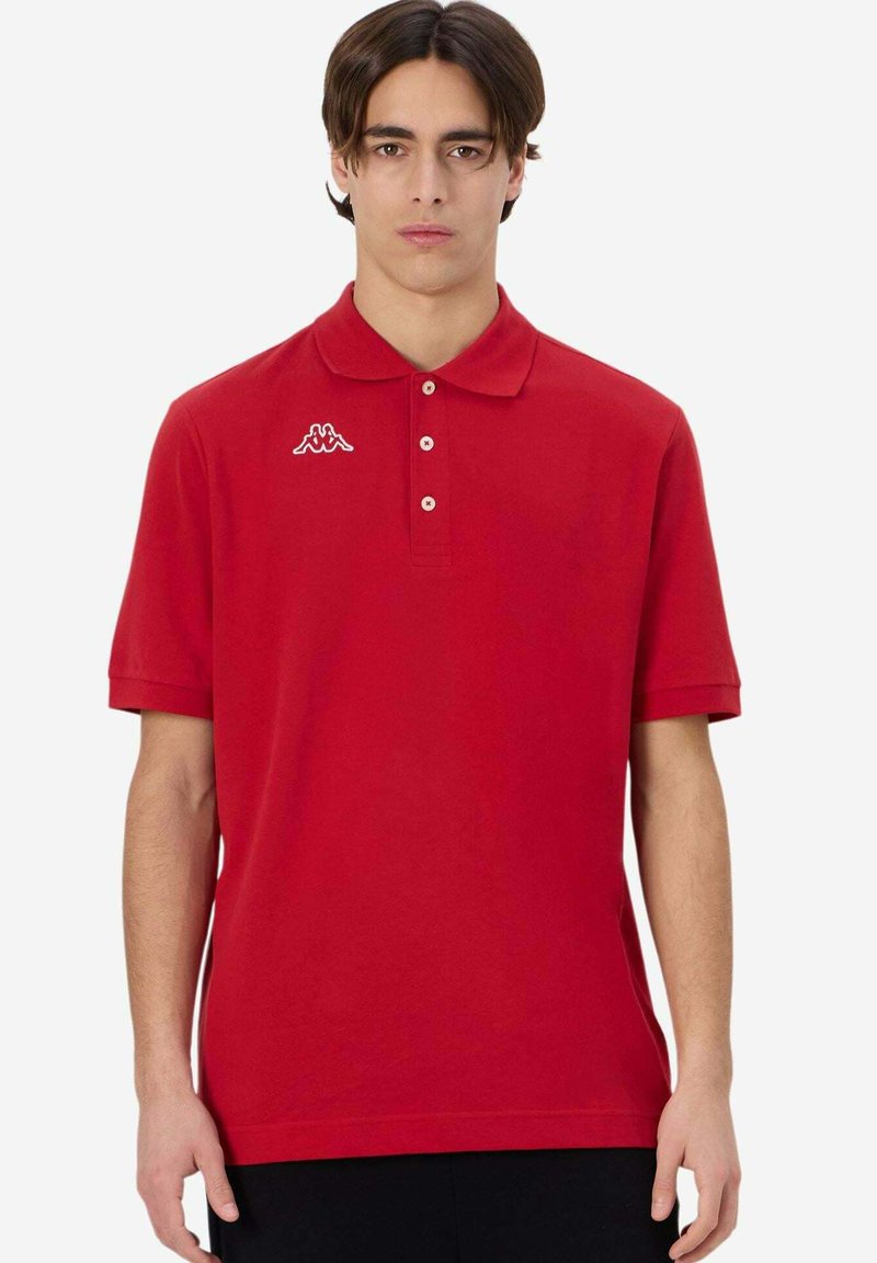 Polo rosso in cotone, con colletto, patta con tre bottoni e logo bianco sul lato sinistro del petto. Maniche corte, texture uniforme.