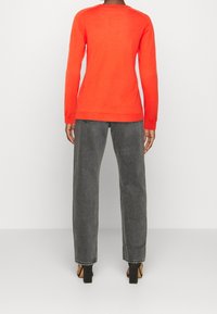 Un pull à manches longues orange vif en doux tricot, associé à un jean gris taille haute et décontracté, et des sandales à talons noires.