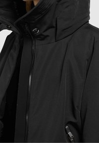 Giacca isolante nera con colletto alto, zip frontale e due tasche laterali. Presenta una texture liscia e un design minimalista.