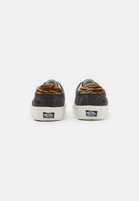 Paire de baskets Vans noires avec semelles blanches, vues de dos, comportant des accents en fourrure rayée tigre marron et noire sur les colliers de talon.