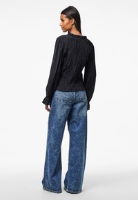 Čierna blúzka so smockovaním a volánovým výstrihom, spárovaná s jasnomodrými širokými džínami s vyblednutou denimovou textúrou a zadnými vreckami.