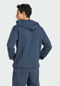 Marineblaue Kapuzenjacke aus weichem Material mit lockerer Passform, ausgestattet mit einer Kängurutasche sowie gerippten Bündchen und Saum.