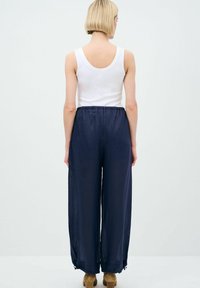 Marineblauwe, loszittende broek van lichtgewicht stof met een elastische tailleband. Geen zichtbare patronen of versieringen.