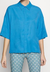 Korte mouwen, button-up shirt van heldere blauwe stof. Heeft een klassieke kraag en een comfortabele pasvorm, gecombineerd met gestreepte blauwe broek.