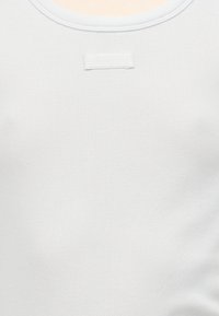 Λευκό ριμπ φανελάκι με ένα μικρό ορθογώνιο πατς με την ετικέτα «JOOP!» τοποθετημένο στο κέντρο κοντά στη γραμμή του λαιμού.