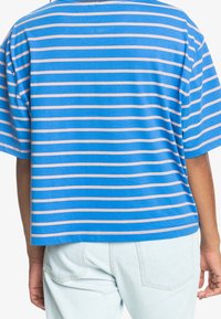 Blå randig t-shirt med horisontella ljusrosa ränder, korta ärmar, rund halsringning och en avslappnad passform, tillsammans med ljusa denim underdelar.