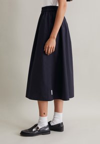Navy midi nederdel lavet af et glat stof, med en elastisk talje og et diskret hvidt mærke, parret med sorte sko og hvide strømper.
