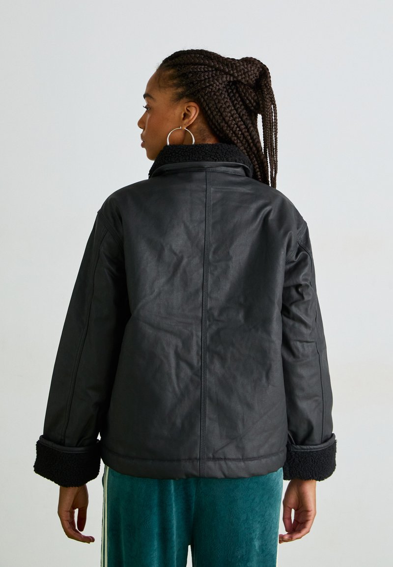 Zwarte neplederen jas met een textuur, fleece-gevoerde kraag en manchetten. Loose fit met een rechte snit en minimale stikseldetails.