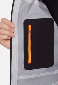 Black and gray jacket interior featuring a zippered pocket with an orange zipper and a black tab, showcasing smooth fabric texture.