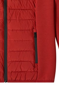 Veste rouge avec panneau avant matelassé et manches en tissu lisse, avec une fermeture éclair noire et une poche zippée sur le côté.