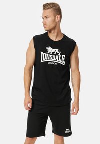 Juodas be Rankovių marškinėlis su baltu liūto grafiku ir užrašu "LONSDALE LONDON", derinamas su juodomis šortais su logotipu.