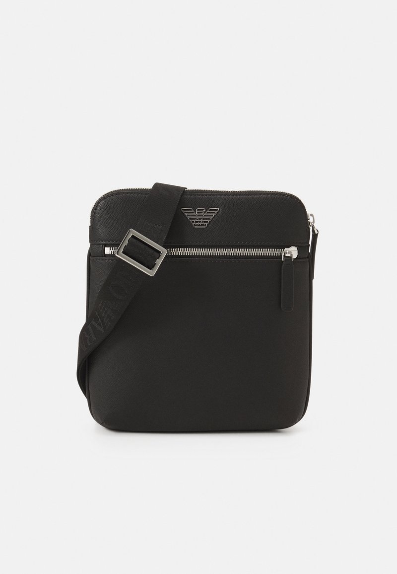 Black crossbody bag made of textured fabric. Features a zippered main compartment, adjustable strap, and embossed logo detail at the front.