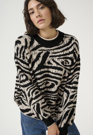 Knit sweater in cream and black zebra pattern, featuring a round black neckline and loose fit. The fabric appears soft with a textured finish.