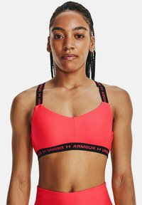 Soutien-gorge de sport rose avec une marque Under Armour noire sur les bretelles et la bande. Texture lisse, conçu pour les vêtements de sport, avec une coupe ajustée.