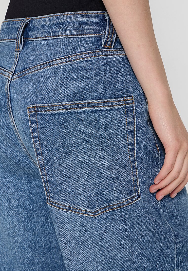 Hellblaue Denim-Jeans mit hoher Taille, ausgestattet mit einer Gesäßtasche und kontrastierenden Nähten. Der Stoff hat ein glattes, leicht strukturiertes Erscheinungsbild.