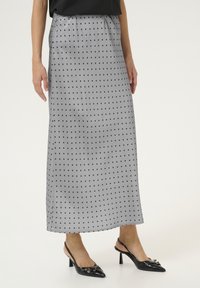 Falda maxi de satén gris con lunares negros, con una cinturilla elástica. Combinada con zapatos de tacón destalonados de punta negra.