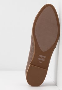Semelle de chaussure en caoutchouc marron avec un motif de grip texturé, présentant le logo "TOMS" et la taille indiquée comme W6½. Bord supérieur lisse avec une forme arrondie.