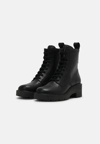 Botas de cuero negras hasta el tobillo con punta redonda, cierre con cordones en la parte delantera, cremallera lateral y suela de plataforma gruesa. Presentan una tira en la parte posterior.