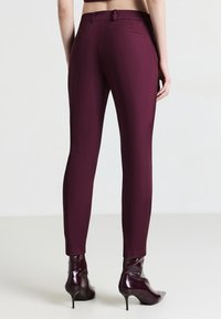 Burgunderfarbene, figurbetonte Hose mit glatter Textur, Gesäßtaschen und mittelhohem Bund, kombiniert mit glänzenden High Heels.