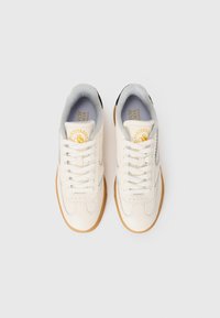 White leather sneakers with a textured finish, grey inner lining, black accents at the heel, and a gum rubber sole. Features flat laces.
