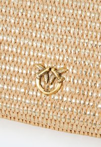 Borsa intrecciata beige con filamenti d'oro lucidi e una chiusura dorata che presenta due uccelli dettagliati che si fronteggiano.