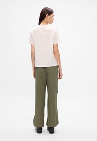 Μπλούζα κοντομάνικη σε ανοιχτό ροζ χρώμα με ίσια γραμμή, συνδυασμένη με ελαιόλαδο πράσινα φαρδιά παντελόνια. Επίπεδα παπούτσια ολοκληρώνουν το σύνολο.