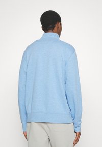 Ljusblå sweatshirt med hög krage, långa ärmar och ribbade muddar. Tillverkad av ett mjukt, strukturerat tyg; avslappnad passform.