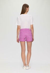 Shorts en denim rose avec une coupe classique, ourlets retroussés et poches arrière. Associés à un t-shirt blanc uni et à des chaussures de couleur claire.