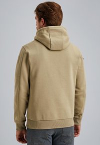 Beige Kapuzenpullover mit weichem Material, gerippten Bündchen und Saum. Hat einen lockeren Schnitt und ein kleines Logo auf der linken Schulter.